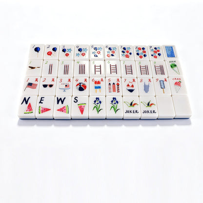A set of white mahjong tiles arranged in a grid on a clean white background. The tiles feature various symbols, numbers, and illustrations including hearts, bars, ladders, flags, flowers, watermelon slices, and the words 'JOKER'.